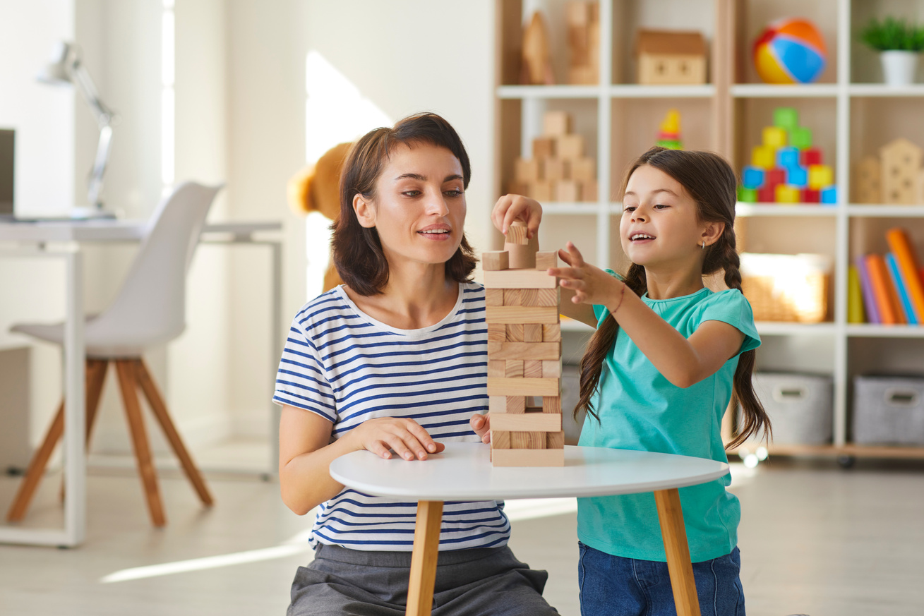 Mom and Daughter Playing and Building Tower Out of Wood Blocks in Cozy Nursery at Home